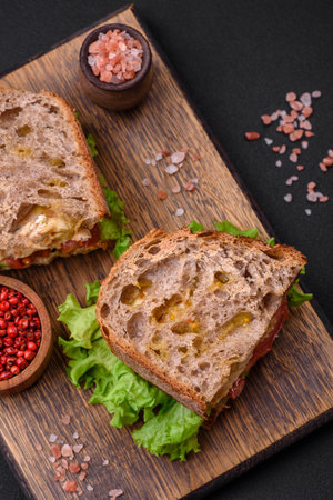 Delicious sandwich with crispy toast, chicken, tomatoes and lettuce on a dark concrete backgroundの写真素材