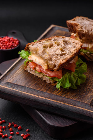 Delicious sandwich with crispy toast, chicken, tomatoes and lettuce on a dark concrete backgroundの写真素材