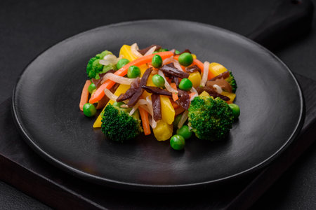 Delicious steamed vegetables broccoli, mushrooms, peas, carrots and onions on a dark concrete backgroundの写真素材