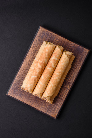 Delicious crispy wafer rolls with cream filling with nuts on a dark concrete background