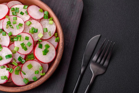 Delicious fresh salad of sliced radishes with green onions, salt and olive oil on a dark concrete backgroundの写真素材