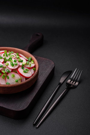 Delicious fresh salad of sliced radishes with green onions, salt and olive oil on a dark concrete backgroundの写真素材