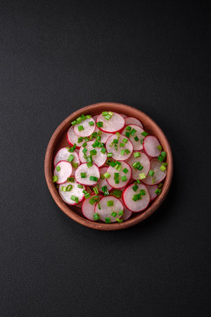 Delicious fresh salad of sliced radishes with green onions, salt and olive oil on a dark concrete backgroundの写真素材