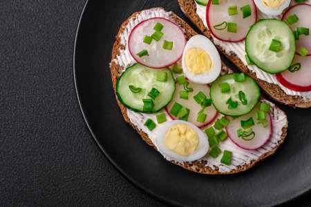 Delicious sandwich or bruschetta with cream cheese radish and green onions on a dark concrete backgroundの写真素材