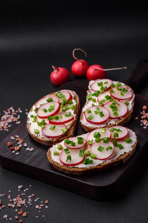 Delicious sandwich or bruschetta with cream cheese radish and green onions on a dark concrete backgroundの写真素材