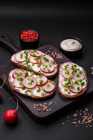 Delicious sandwich or bruschetta with cream cheese radish and green onions on a dark concrete backgroundの写真素材