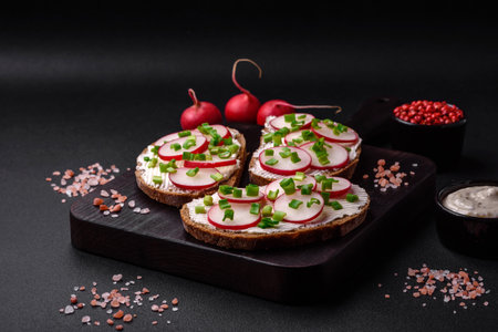 Delicious sandwich or bruschetta with cream cheese radish and green onions on a dark concrete backgroundの写真素材