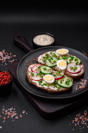Delicious sandwich or bruschetta with cream cheese radish and green onions on a dark concrete backgroundの写真素材
