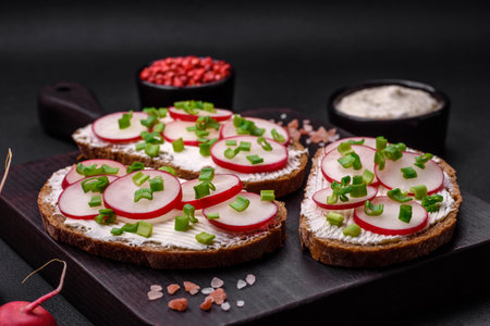 Delicious sandwich or bruschetta with cream cheese radish and green onions on a dark concrete backgroundの写真素材