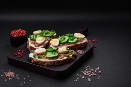 Delicious sandwiches consisting of grilled toast, canned tuna, cream cheese, cucumber and boiled quail eggs on a dark concrete backgroundの写真素材