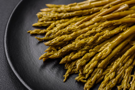 Sprigs of delicious canned asparagus on a black ceramic plate on a dark concrete backgroundの写真素材