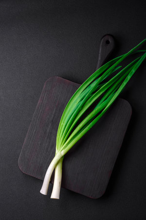 Fresh green onions on a wooden rectangular cutting board on a dark concrete backgroundの写真素材