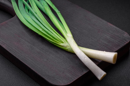 Fresh green onions on a wooden rectangular cutting board on a dark concrete backgroundの写真素材