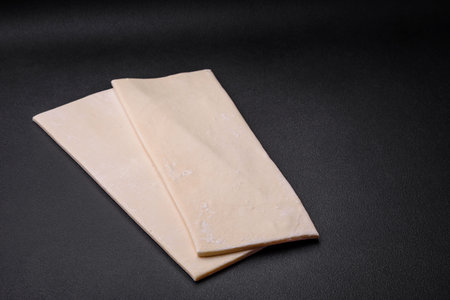 Sheets of raw puff pastry on a dark concrete background. Cooking sweet pastries at home