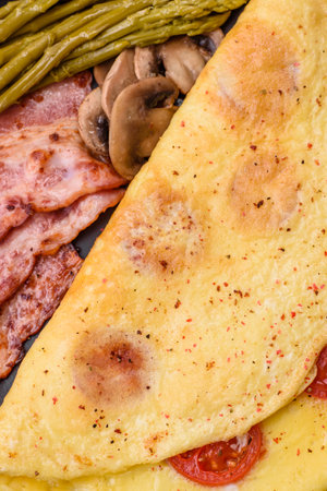 Delicious fresh omelet with cherry tomatoes, bacon, asparagus and spices on a dark concrete...