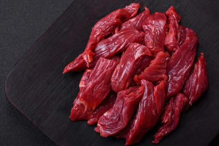 Fresh raw beef with salt, spices and herbs on a dark concrete background