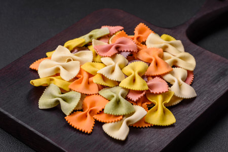 Raw farfalle pasta in different colors on a dark concrete background. Preparing to cook Italian foodの写真素材