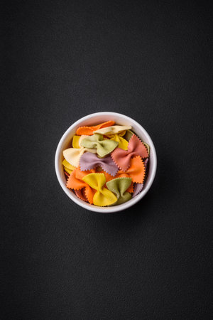 Raw farfalle pasta in different colors on a dark concrete background. Preparing to cook Italian foodの写真素材