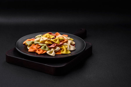 Raw farfalle pasta in different colors on a dark concrete background. Preparing to cook Italian foodの写真素材