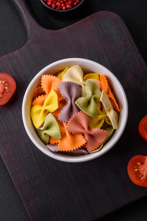 Raw farfalle pasta in different colors on a dark concrete background. Preparing to cook Italian foodの写真素材