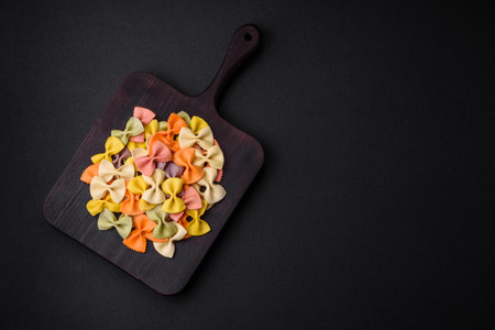 Raw farfalle pasta in different colors on a dark concrete background. Preparing to cook Italian foodの写真素材