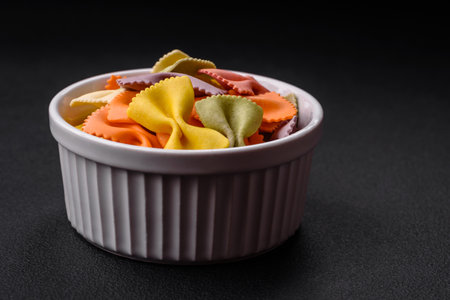 Raw farfalle pasta in different colors on a dark concrete background. Preparing to cook Italian foodの写真素材