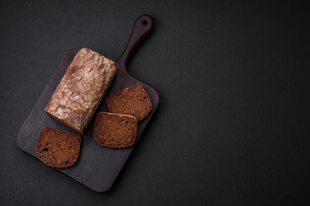 Loaf of fresh crispy brown bread with grains and seeds on dark concrete backgroundの写真素材