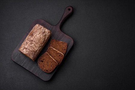 Loaf of fresh crispy brown bread with grains and seeds on dark concrete backgroundの写真素材