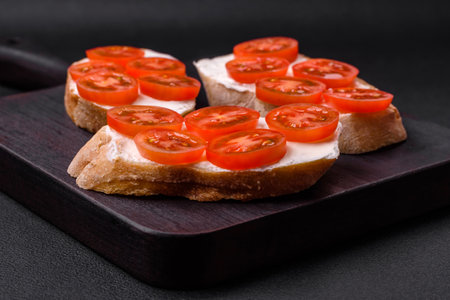 Delicious crispy grilled toast with cheese and cherry tomatoes on a dark concrete backgroundの写真素材