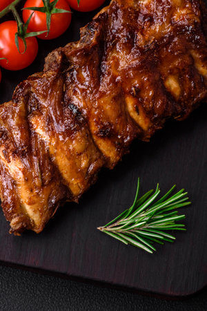 Delicious grilled pork ribs with sauce, spices and herbs on a dark concrete background