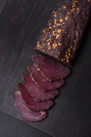 Delicious smoked Armenian basturma with spices and herbs sliced on a dark concrete backgroundの写真素材