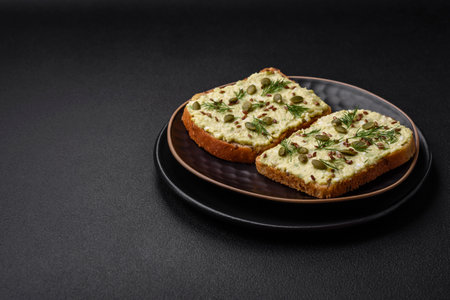 Grilled toast with avocado paste, eggs, cream cheese, salt, spices and herbs on a textured concrete...