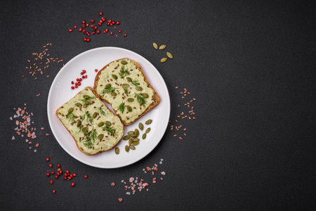 Grilled toast with avocado paste, eggs, cream cheese, salt, spices and herbs on a textured concrete...