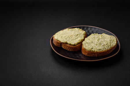 Grilled toast with avocado paste, eggs, cream cheese, salt, spices and herbs on a textured concrete tableの写真素材