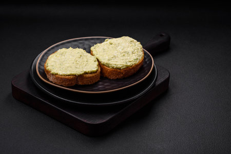 Grilled toast with avocado paste, eggs, cream cheese, salt, spices and herbs on a textured concrete tableの写真素材