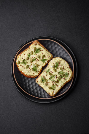 Grilled toast with avocado paste, eggs, cream cheese, salt, spices and herbs on a textured concrete...