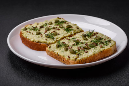 Grilled toast with avocado paste, eggs, cream cheese, salt, spices and herbs on a textured concrete tableの写真素材