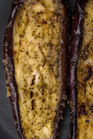 Delicious eggplant cut into two halves baked with salt, spices and herbs on a dark concrete backgroundの写真素材