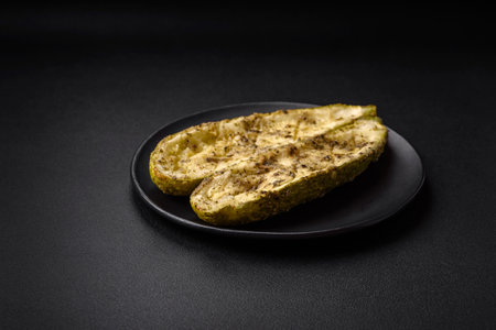 Delicious zucchini cut into two halves baked with salt, spices and herbs on a dark concrete backgroundの写真素材
