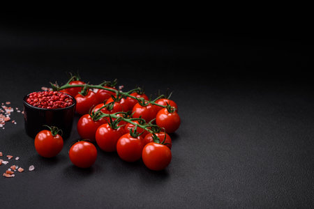 Delicious fresh cherry tomatoes on a twig with spices and herbs on a dark concrete backgroundの写真素材