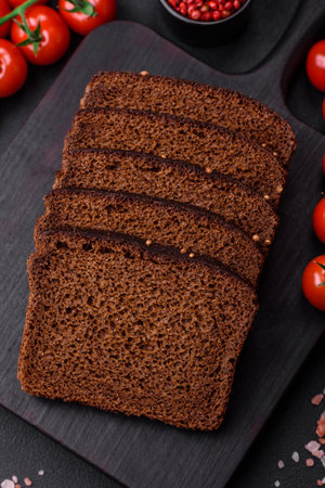 Delicious fresh brown bread with grains and seeds sliced on a wooden cutting board on a dark...