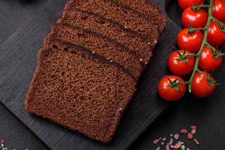 Delicious fresh brown bread with grains and seeds sliced on a wooden cutting board on a dark...