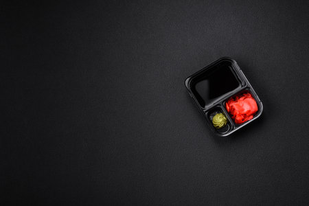 Pickled ginger, soy sauce and wasabi in portioned plastic containers on a dark concrete backgroundの写真素材