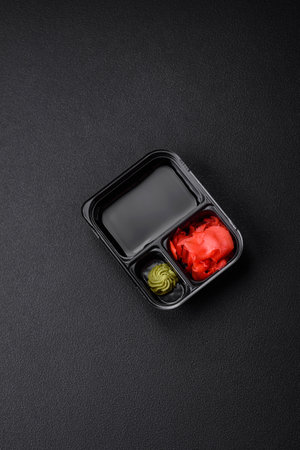 Pickled ginger, soy sauce and wasabi in portioned plastic containers on a dark concrete backgroundの写真素材
