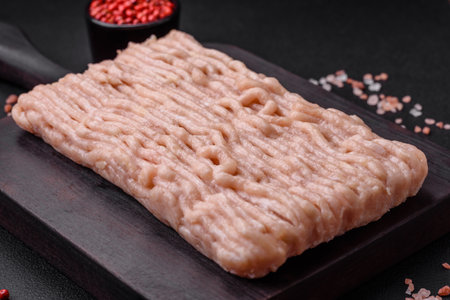 Fresh minced chicken with salt, spices and herbs on a wooden cutting board on a dark concrete...