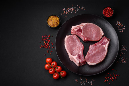 Raw pork on the bone or rib sliced with salt, spices and herbs on a dark concrete backgroundの写真素材