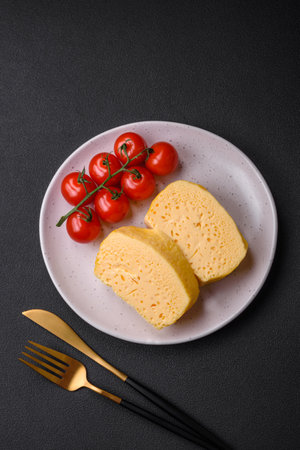 Delicious omelet with milk, spices and herbs cut into large pieces on a ceramic plate on a dark concrete backgroundの写真素材