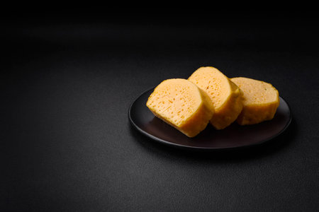 Delicious porous yellow cheese cut in large pieces on a ceramic plate on a dark concrete background