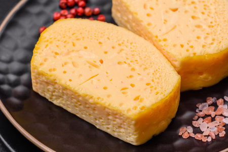Delicious porous yellow cheese cut in large pieces on a ceramic plate on a dark concrete background