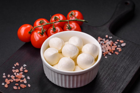 Delicious fresh mozzarella cheese in the form of small balls with salt and spices on a dark concrete backgroundの写真素材